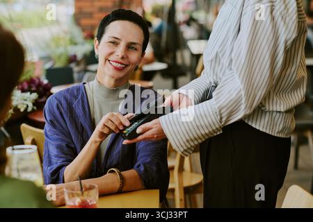 Frau mittleren Alters lächelt, während sie mit Kreditkarte bezahlt Stockfoto