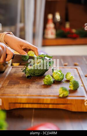 Nahaufnahme der Hände, die frischen Brokkoli auf Holzbrett in der gemütlichen rustikalen Küche schneiden Stockfoto