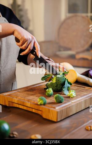 Nahaufnahme der Hände, die frischen Brokkoli auf Holzbrett in der gemütlichen rustikalen Küche schneiden Stockfoto