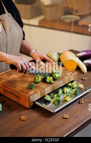 Frischer Brokkoli wird auf einem hölzernen Schneidebrett in gemütlicher Küche geschnitten Stockfoto