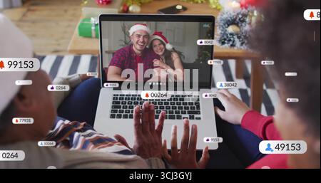 Winkende afroamerikanische Frauen begrüßen das Weihnachtsmannspaar mit einem Laptop zu Hause mit Streaming-Alerts. Festlich, feierlich, digital, saisonal, warm, Stockfoto