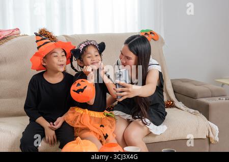 Eine Frau macht mit ihrem Handy ein Foto von zwei Kindern in Kostümen, einem Jungen mit orangefarbenem Hut Stockfoto