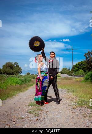 Das junge mexikanische Paar trägt Folklore-Kostüme, mit dem Mann in einem schwarzen charro-Mariachi-Anzug und der Frau in einem lebendigen, bestickten Rock, Celebratin Stockfoto
