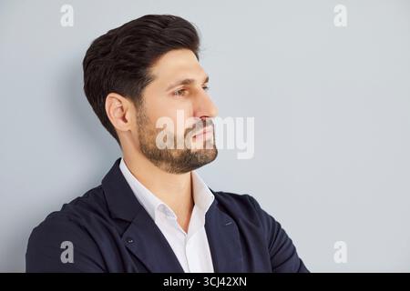Porträt eines selbstbewussten jungen Geschäftsmannes mit formellem Anzug, der auf grauem Wandhintergrund steht Stockfoto