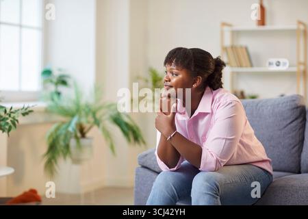 Glückliche Afroamerikanerin, die zu Hause auf dem Sofa sitzt Stockfoto