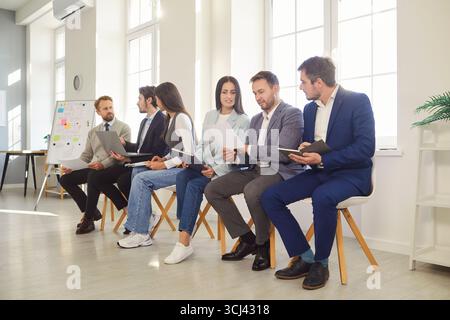 Ein Team von Büroangestellten sitzt in einer Reihe auf bequemen Stühlen und diskutiert etwas Stockfoto