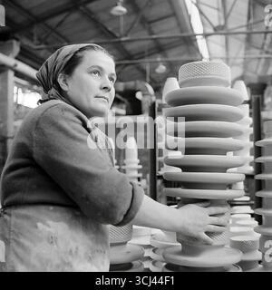 Eine erfahrene sowjetische Arbeiterin mit inspiriertem Gesicht inspiziert Ende der 1950er Jahre in einer Werkstatt im Werk Sloviansk fertige Isolatoren Das Archivporträt eines Arbeiterveteranen im Stil des sozialistischen Realismus vermittelt ein Gefühl der würde und des Glaubens an eine glänzende Zukunft. Dieses Bild einer Weise arbeitenden Frau ist ein Symbol für die kreative Kraft und das friedliche Leben des Donbas und fängt die verlorene Ära vor dem Krieg ein Stockfoto