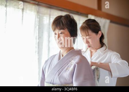 Eine Frau im Kimono wird von einer anderen Frau dabei unterstützt, ihre Kleidung anzupassen. Betreuungs- und Betreuungskonzept der beiden Frauen Stockfoto