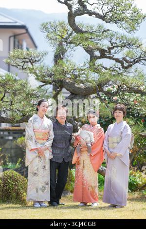 Eine vierköpfige Familie, darunter ein Mann und ein Baby, posieren für ein Bild vor einem großen Baum. Die Familienmitglieder tragen alle traditionelle Japane Stockfoto