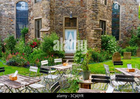 Hattingen, Deutschland - 14. Juni 2025: Malerische Café-Szene im Freien mit rustikalen Holztischen und lebendigem Garten in Hattingen. Stockfoto