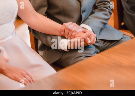 Nahaufnahme eines Paares, das während der Hochzeitszeremonie die Hände hält. Der Bräutigam trägt einen Anzug, während die Braut ein weißes Kleid trägt. In diesem Moment Stockfoto