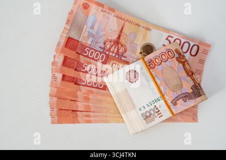 Russische Währung auf einer weißen Oberfläche mit mehreren Stückelungen und Noten von 5000 Rubel in verschiedenen Richtungen Stockfoto