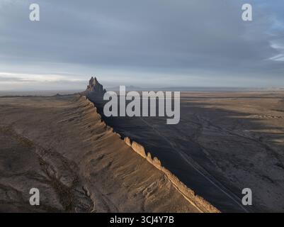 Aus der Vogelperspektive der imposanten Shiprock-Formation, die lange Schatten über die trockene Landschaft unter einem ruhigen Himmel wirft, Shiprock, New Mexico, USA. Stockfoto