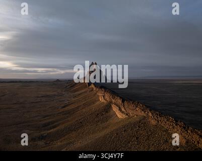 Die imposante Shiprock-Formation aus der Vogelperspektive bildet eine dramatische Figur vor der riesigen, trockenen Landschaft unter einem glühenden Himmel in New Mexico, USA. Stockfoto