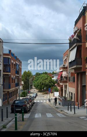 Viladecans. Barcelona - 5. September 2025: Blick nach unten auf eine steile Straße, die von Gebäuden flankiert wird. Ein dunkler, stürmischer Himmel schafft ein dramatisches, filmisches, Stockfoto