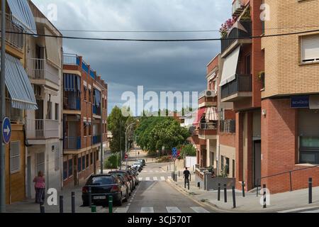 Viladecans. Barcelona - 05. September 2025: Ein einsamer Radfahrer fährt eine ruhige Wohnstraße hinunter, während ein Sturm sich über sich sammelt. Das Bild weckt Gefühle Stockfoto