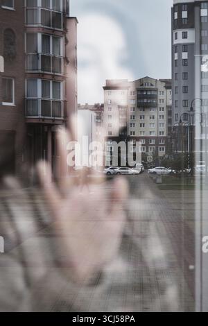 Traurige einsame junge Frau, die durch das Fenster auf die moderne Stadt blickt Stockfoto