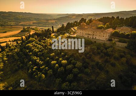 Panoramablick auf ein großes altes Anwesen auf einem Hügel mit Blick auf die Olivenhaine und Weinberge in der wunderschönen, im Spätsommer toskanischen Landschaft, Italien Stockfoto
