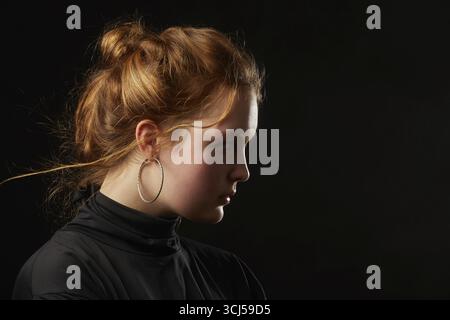Ernste traurige junge Frau mit Down-Syndrom auf schwarzem Hintergrund-Seitenprofilansicht Stockfoto