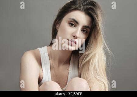 Junge traurige Frau in weißem Hemd posiert auf grauem Hintergrund Stockfoto