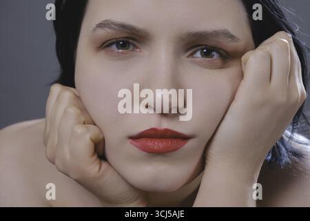 Trauriges weibliches Nahaufnahme-Porträt. Junge nachdenkliche Frau, die auf grauen Hintergrund in die Kamera schaut Stockfoto