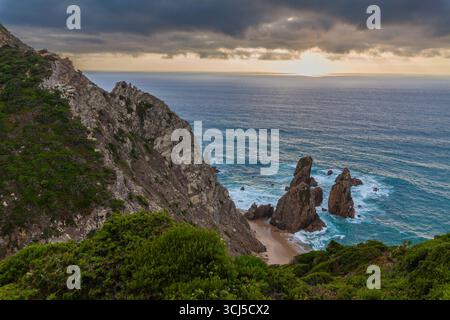 Eine atemberaubende Küstenszene von Praia da Ursa mit dramatischen Klippen, türkisfarbenem Wasser und Meeresstapeln unter einem goldenen Sonnenuntergang Stockfoto