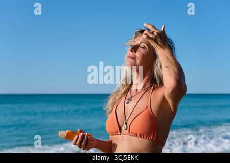 Reife Frau, die am Strand Sonnencreme auf die Stirn aufträgt Stockfoto