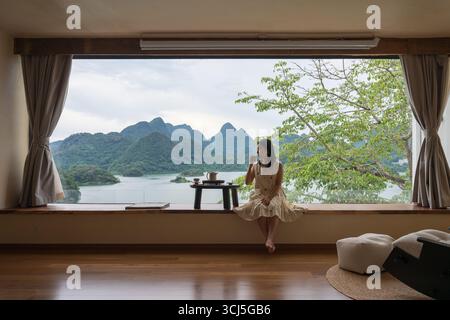 Die Frau saß auf der Fensterbank und trank Tee, mit einer wunderschönen Aussicht vom Fenster. Stockfoto
