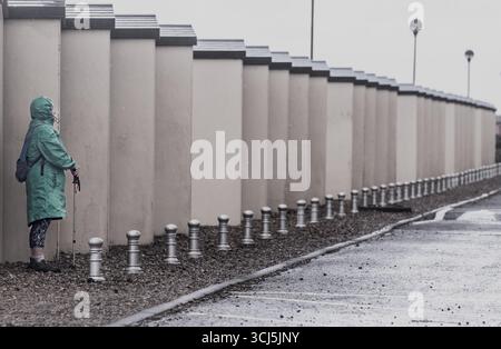 Eine Frau versteckt sich hinter den Strandhütten an der Seaford Promenade vor den Elementen, da raue See und 45 km/h Wind mit starken Regengüssen das Gefühl erwecken, dass es verschwunden ist Stockfoto