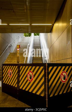 Defekter Escalator am Eingang zu Einer U-Bahn-Station. Eine provisorische Barriere mit gelb-schwarzen Warnstreifen und roten „kein Betreten“-Schildern Stockfoto