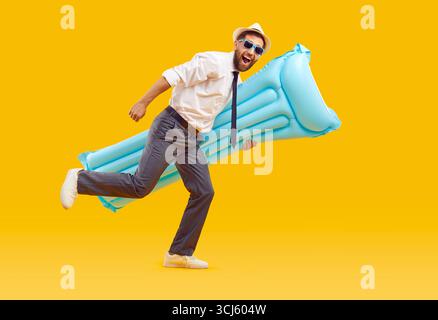 Glücklicher, lustiger Büroangestellter, der Strandmatratze hält und auf gelbem Hintergrund läuft Stockfoto