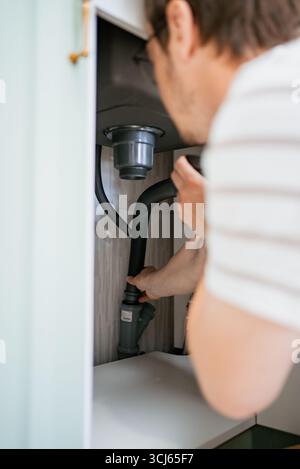 Klempner verbinden Siphonrohr mit Abflussrohr für Spülbecken mit Präzision, um eine effektive Wasserableitung zu gewährleisten und Leckagen in einer eleganten, modernen Küchenumgebung zu verhindern Stockfoto