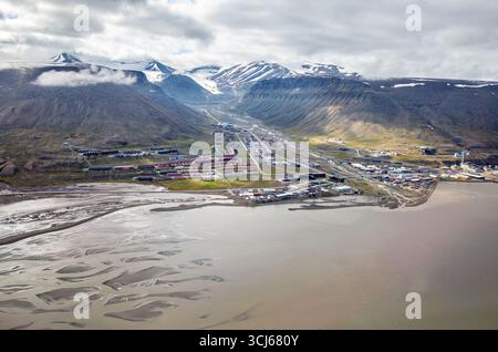 Longyearbyen Aerial View with Mountains and Fjord Svalbard Norwegen // LONGYEARBYEN, Svalbard — eine Luftaufnahme zeigt die Siedlung Longyearbyen, eingebettet zwischen steilen, schneebedeckten Bergen und einem Fjord. Die Stadt liegt auf der Insel Spitzbergen im Svalbard-Archipel und ist Norwegens nördlichste Siedlung. Die Landschaft besteht aus einem geflochtenen Flusssystem, das ins Meer fließt, mit farbenfrohen Gebäuden der Stadt, die sich entlang des Talbodens verteilen. Longyearbyen dient als Verwaltungszentrum von Svalbard und ist ein Drehkreuz für Tourismus, Forschung und Bergbau. Die umliegende Halterung Stockfoto