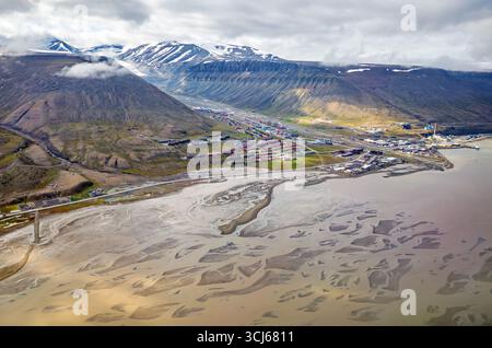 Longyearbyen Aerial View Svalbard Norwegen // LONGYEARBYEN, Svalbard und Jan Mayen — eine Luftaufnahme zeigt die Siedlung Longyearbyen, das größte Siedlungs- und Verwaltungszentrum von Svalbard, Norwegen, während ein Flugzeug sich dem Flughafen nähert. Die Stadt liegt eingebettet in ein Tal mit schneebedeckten Bergen und Gletschern, die eine dramatische Kulisse bilden. Die Landschaft hat ein geflochtenes Flussbett, das zum Meer führt, mit den bunten Gebäuden der Stadt entlang der Küste und den Talhängen. Longyearbyen liegt auf der Insel Spitzbergen und ist die nördlichste Siedlung ihrer Größe Stockfoto