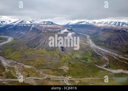 Snowy Mountains und Täler östlich von Longyearbyen Svalbard Norwegen / LONGYEARBYEN, Svalbard und Jan Mayen — schneebedeckte Berge und Gletschertäler werden von einem Flugzeug aus gesehen, das sich dem Flughafen Longyearbyen nähert. Die Landschaft mit gewundenen Flüssen und verstreuten Gebäuden ist charakteristisch für das arktische Gelände der Insel Spitzbergen. Svalbard ist ein Archipel im Arktischen Ozean, auf halbem Weg zwischen dem norwegischen Festland und dem Nordpol, und wurde durch das Svalbard Act von 1925 integraler Bestandteil des Königreichs Norwegen. Longyearbyen liegt bei 78°13'N entlang des Adventfjorden und ist die größte Siedlung Stockfoto