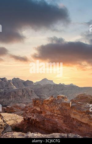 Die Sonne untergeht hinter zerklüfteten Berggipfeln und strahlt ein warmes Leuchten über die felsige Landschaft. Einzigartige Felsformationen stehen im Kontrast zum farbenfrohen Himmel cre Stockfoto