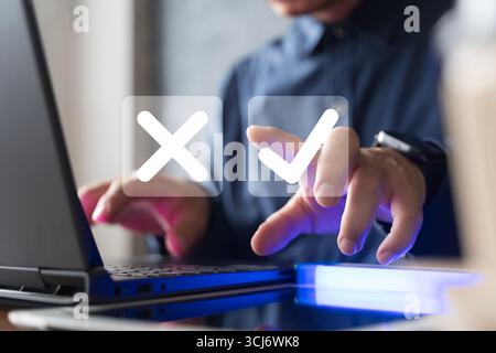 Nahaufnahme der Hand eines Geschäftsmannes mit Laptop mit digitalem Häkchen und Kreuzsymbolen, die Entscheidungsfindung, Genehmigung, Ablehnung, Online-Umfrage symbolisieren fe Stockfoto