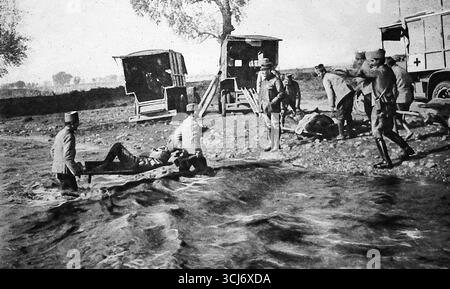 Archivbild aus Le Miroir, 1916, das serbische Soldaten zeigt, die während des Ersten Weltkriegs verwundete Kameraden über den Fluss Brod trugen. Der geschwollene Fluss, der durch schwere Regenfälle für Krankenwagen unpassierbar gemacht wurde, zwang die Evakuierung per Hand. Im Hintergrund stehen die Wagen des Roten Kreuzes bereit, die Verletzten aufzunehmen. Die Szene veranschaulicht die harte Realität der medizinischen Versorgung auf dem Schlachtfeld und die Entschlossenheit der serbischen Streitkräfte während des Balkankampfes im Ersten Weltkrieg. Stockfoto