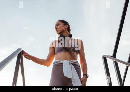 Flacher Blick auf junge, schlanke Frau in Sportbekleidung, die auf der Treppe auf dem Dach steht und wegblickt Stockfoto