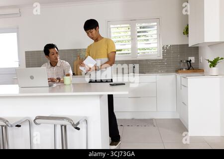 Asiatische Männer diskutieren in der modernen Küche mit Laptop und Notizblock Stockfoto