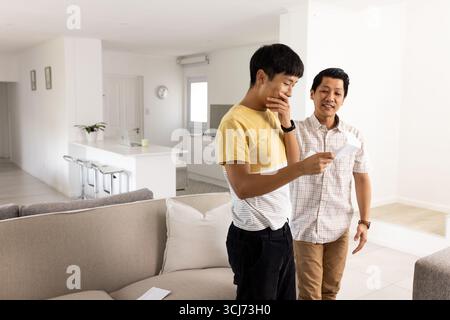 Junger Mann liest Brief, während ein lächelnder Freund in der Nähe im modernen Wohnzimmer steht Stockfoto