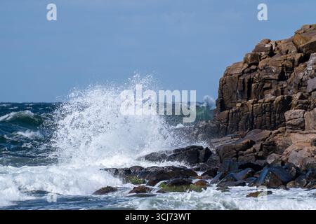 Wellen krachen gegen eine felsige Küste, Seewasser und Wildwasser unter blauem Himmel Stockfoto