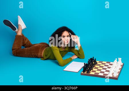 Junge Frau spielt Schach, während sie sich auf einem farbenfrohen Hintergrund entspannt und strategisches Denken und Freizeitaktivitäten demonstriert Stockfoto
