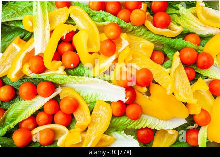 Frischer Salat aus ganzen Kirschtomaten, in Scheiben geschnittenen gelben Paprika und Salatblättern. Stockfoto