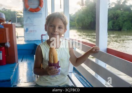Kind, isst Sandwich auf einer Bootsfahrt in Vietnam, im Sommer Stockfoto
