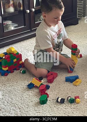 Ein dreijähriger Junge spielt glücklich mit Legos im Wohnzimmer eines Wohnhauses, 2025, USA Stockfoto