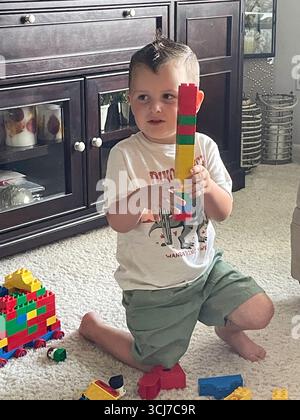 Ein dreijähriger Junge spielt glücklich mit Legos im Wohnzimmer eines Wohnhauses, 2025, USA Stockfoto