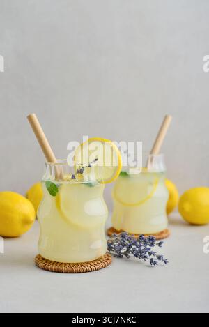 Zwei Gläser hausgemachte Lavendellimonade mit Trinkhalmen, frischen Zitronen und Minze auf hellem Hintergrund Stockfoto