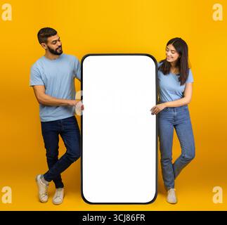 Coole mobile App. Millennial arabische Ehepartner stehen neben einem riesigen Smartphone mit Mockup, Werbung für App oder Website Stockfoto