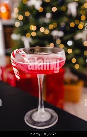 Cranberry-Cocktail garniert mit einem Zuckerrohr in einem Glas, vor einem verschwommenen Hintergrund von Weihnachtslichtern und -Dekorationen. Stockfoto
